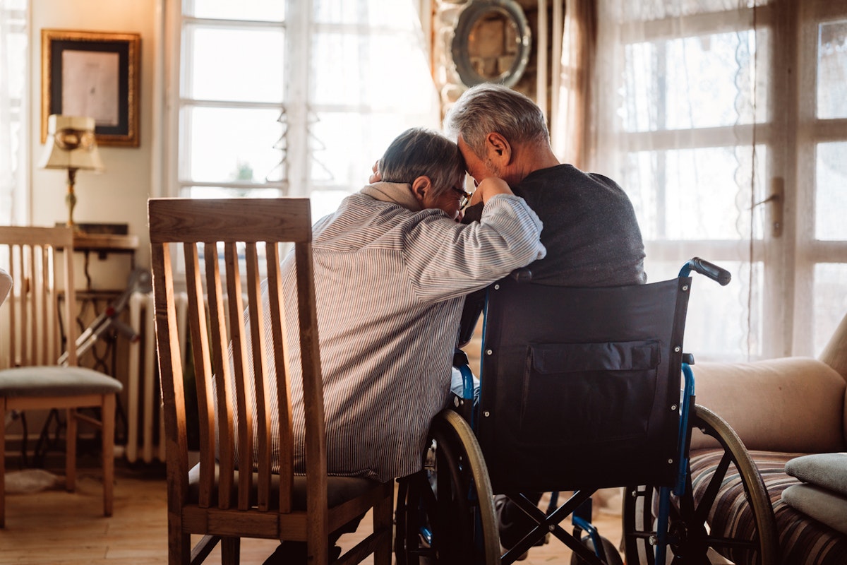 A woman siting on a chair next to her husband in a wheelchair